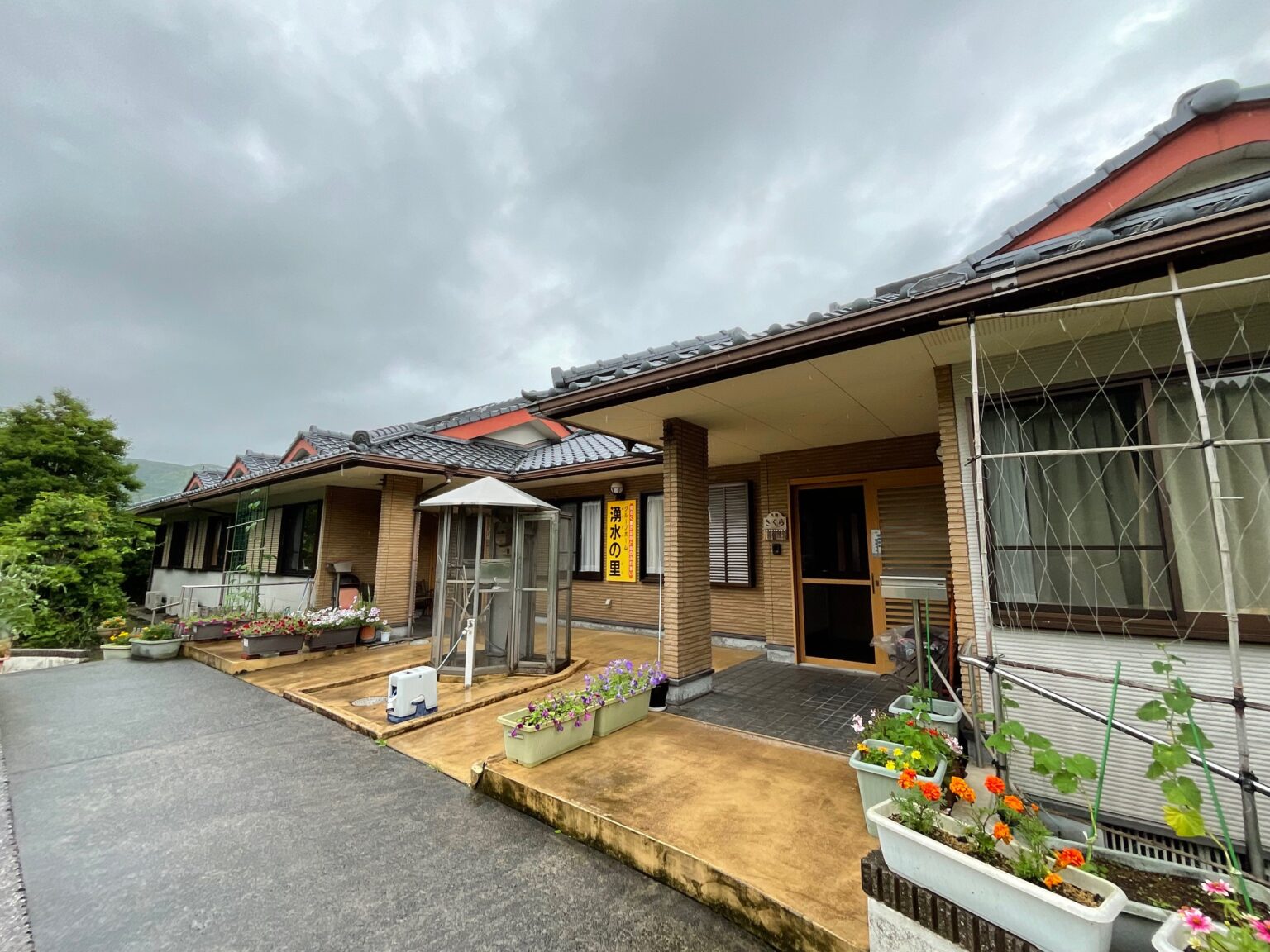 赤い屋根の介護施設外観。木製デッキと花壇が配置された入口周辺